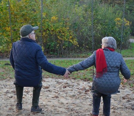 Elderly couple holding hands on swings